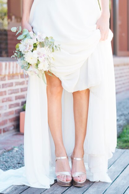 Low section of a bride holding flower bouquet in hand showing her fashionable high heels