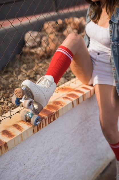 Low section of a female skater sitting near the fence