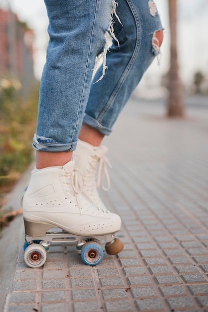 Low section of a female skater in white roller skate standing on sidewalk