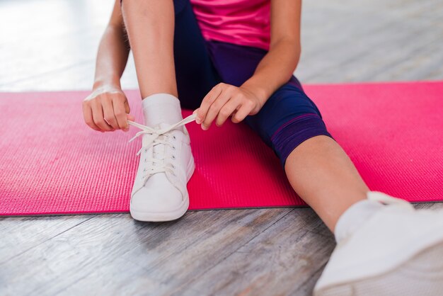 Low section of a girl sitting on exercise mat tying shoelace