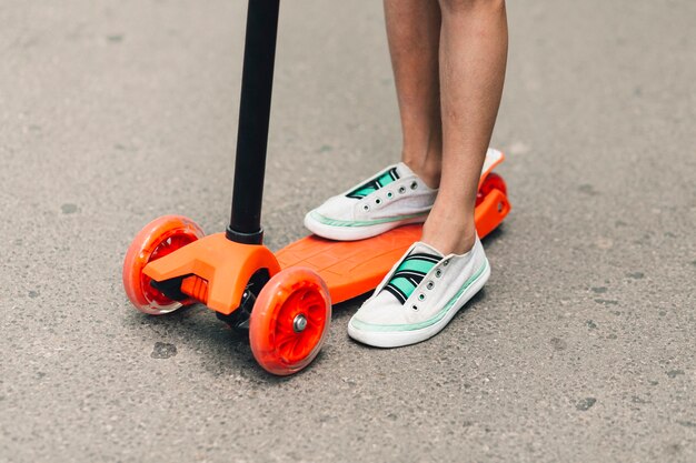 通りのオレンジプッシュスクーターに立っている女の子の低いセクション