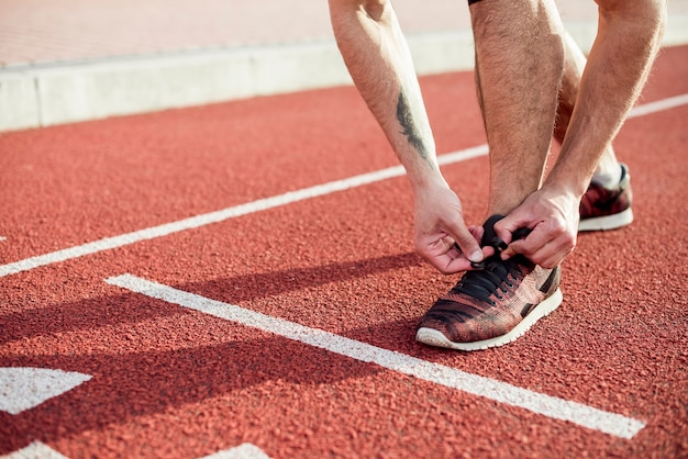 Sezione bassa dell'atleta maschio sulla linea di partenza legando il laccio sulla pista da corsa