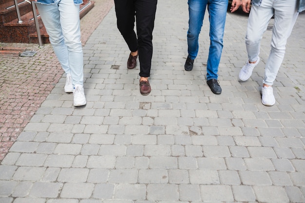 Low section of male friends walking together on pavement