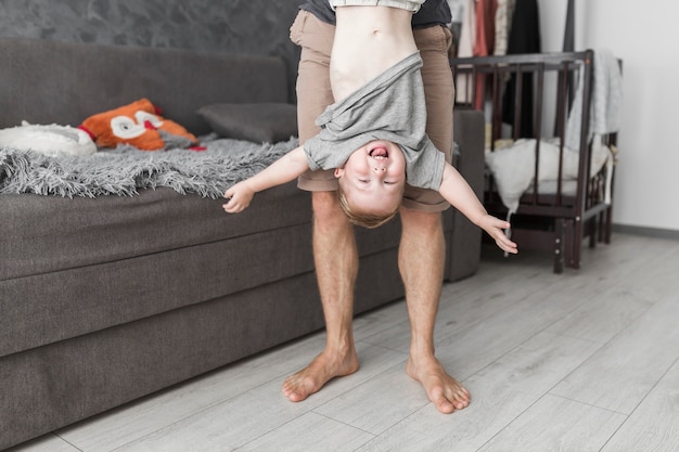 Foto gratuita sezione bassa di un uomo che tiene suo figlio sottosopra a casa