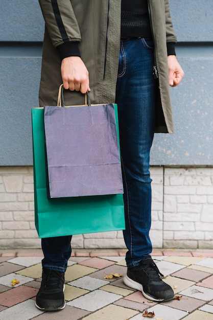 カラフルな買い物袋を手で押し舗装の上に立っている人の低いセクション