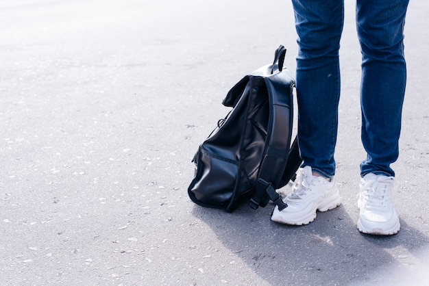 Low section of a person standing on street with black backpack