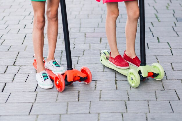 Low section of two girls standing on kick scooter