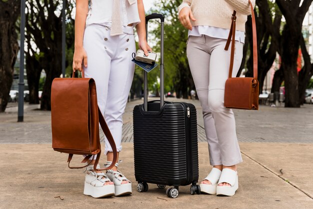 검은 가방과 가죽 가방으로 서있는 두 젊은 여성의 낮은 섹션