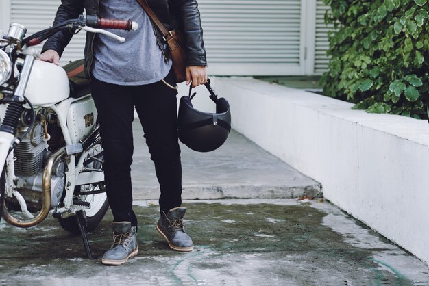 Низкая часть неузнаваемого байкера, держащего шлем, стоящего у его белого мотоцикла