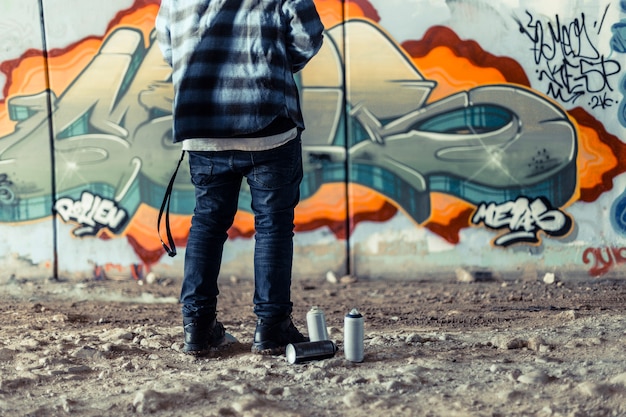 Low section view of artist standing near spray can in front of graffiti on wall