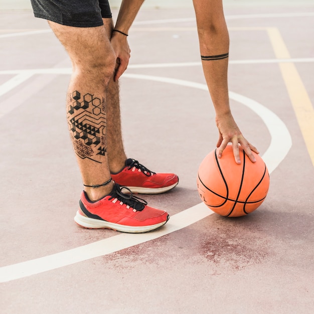 Low section view of a man picking up basketball in court