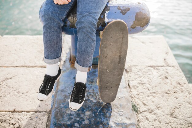 ボラードに座っているスケートボードを持つ男の低断面図