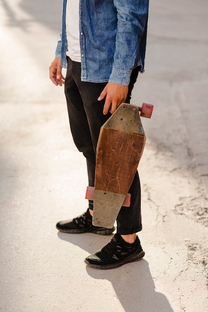 木製のスケートボードを持つ男の低断面図
