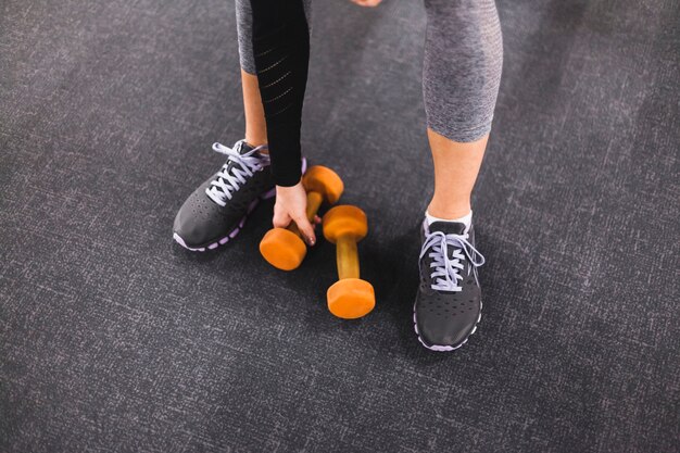 Low section view of a woman picking dumbbell in gym