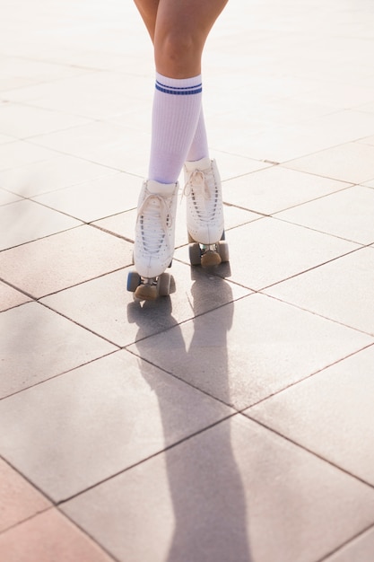 Sezione bassa della donna in roller skate in piedi con le gambe incrociate sul pavimento