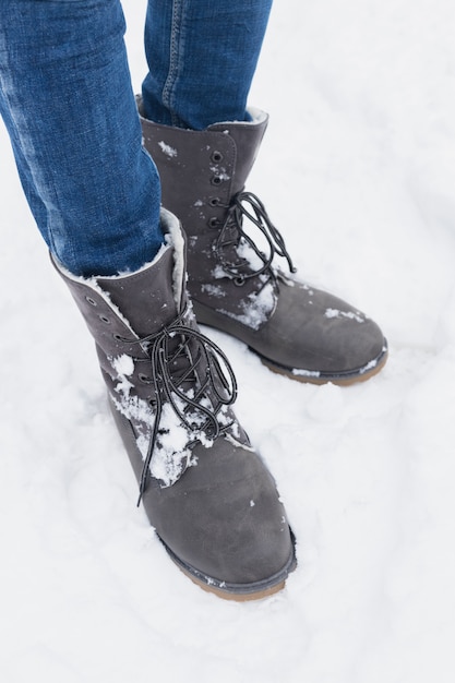 雪の中で冬のブーツと立っている女性の低いセクション