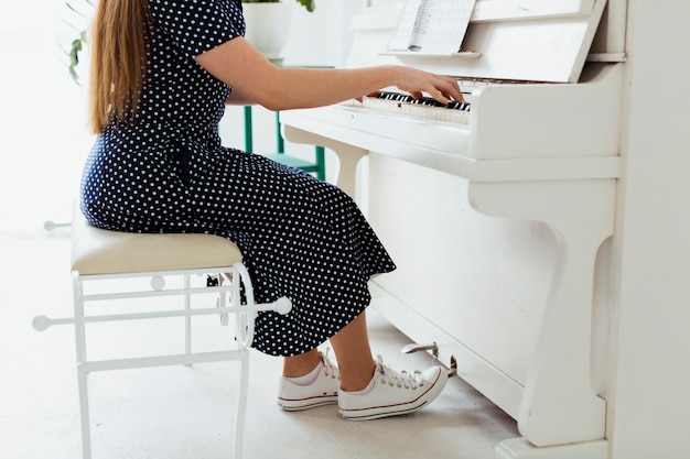 Foto gratuita sezione bassa di una giovane donna che indossa scarpe di tela suonare il pianoforte