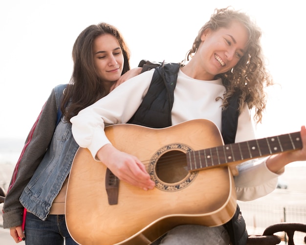 Low view female friends playing the guitar