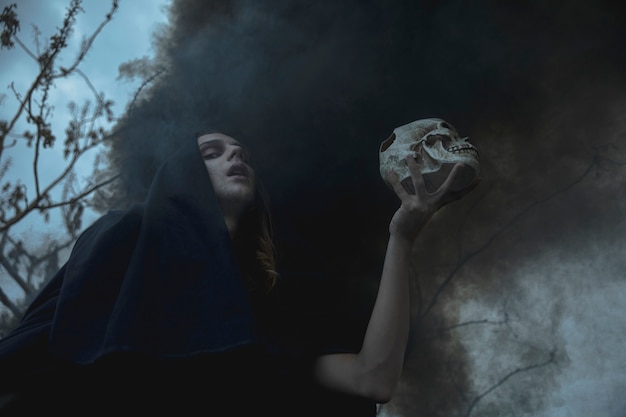 Free photo low view man holding a skull in black fog