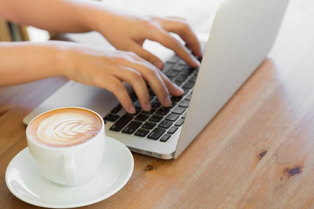 Lperson working on a laptop with a cup of coffee next