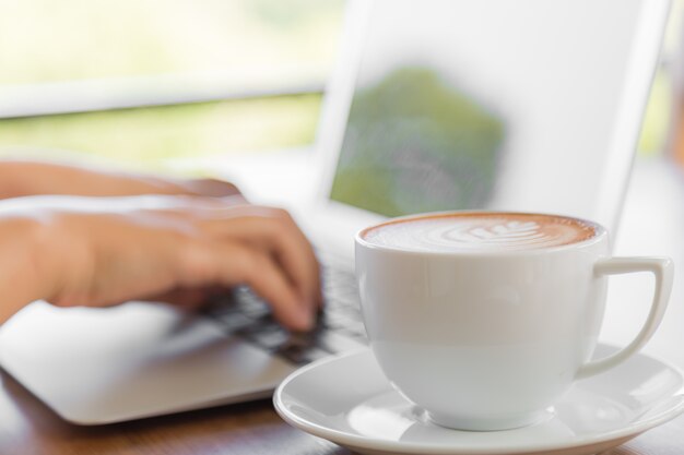 Lperson working on a laptop with a cup of coffee next