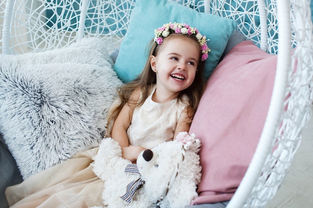 Luaghing girl sits in round chair with toy bear on her knees