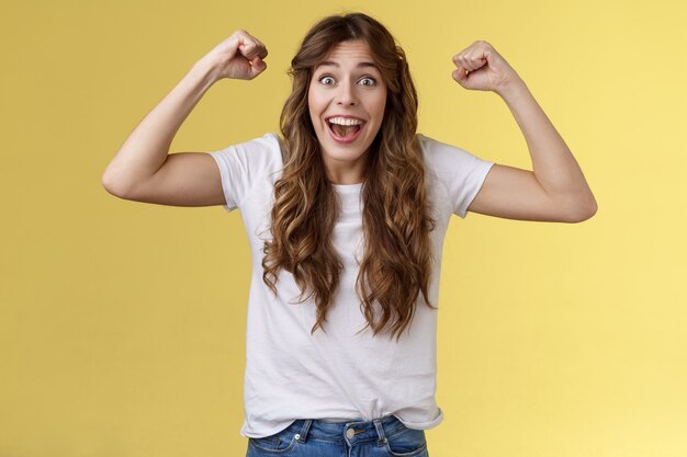 Lucky girl feeling like winner. Triumphing excited cheerful young woman raise hands fist pump up celebratory smiling broadly thrilled yelling supportive root favorite team reach success.