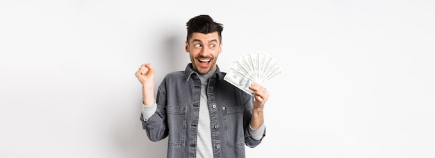 Free photo lucky man winning prize money and scream of excitement staring at dollar bills happy standing on whi