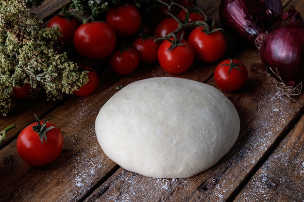 Lump of dough on a wooden table surrounded with tomatoes and onions