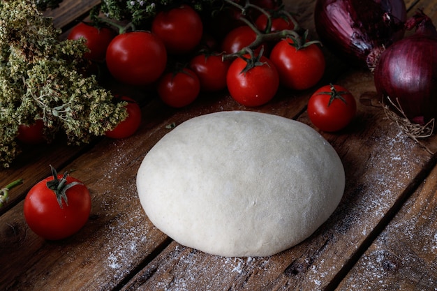 Foto gratuita pezzo di pasta su un tavolo di legno circondato da pomodori e cipolle