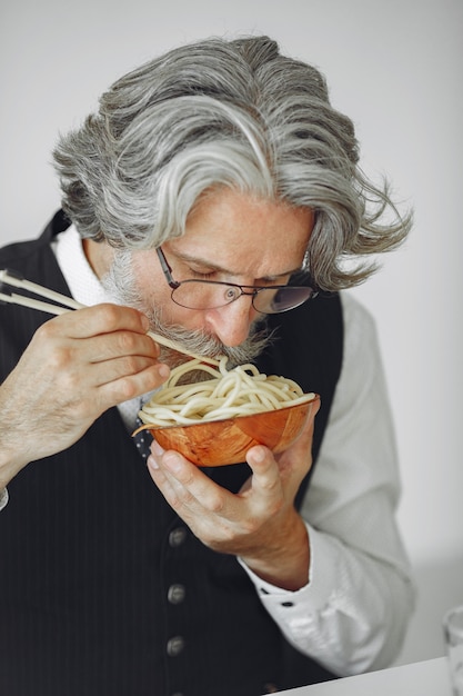 Foto gratuita pausa pranzo. uomo elegante in ufficio. uomo d'affari in camicia bianca. l'uomo mangia le tagliatelle.