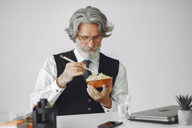 昼休み。オフィスでエレガントな男。白いシャツのビジネスマン。男は麺を食べる。