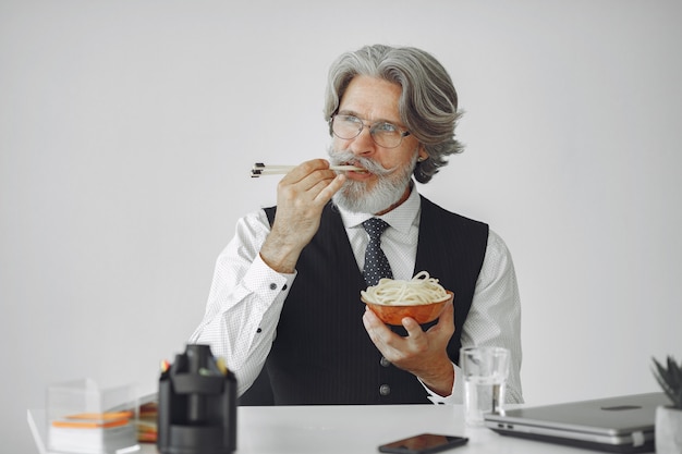 Lunch break. Elegant man in office. Businessman in white shirt. Man eats noodles.