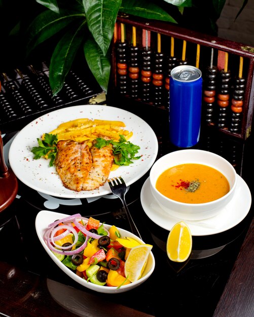 A lunch setup with lentil soup grilled fish and chips and vegetable salad