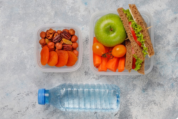 Lunchbox con sandwich, verdure, frutta su bianco.