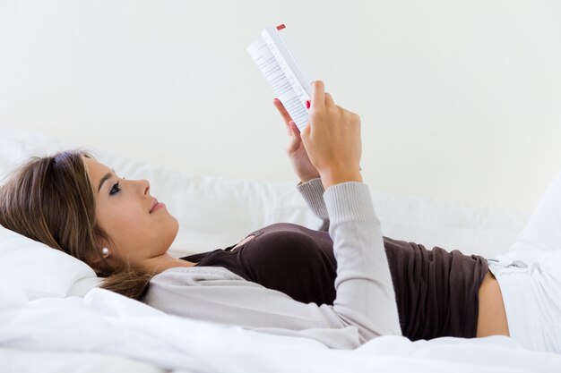 Lying beautiful woman reading book at home.