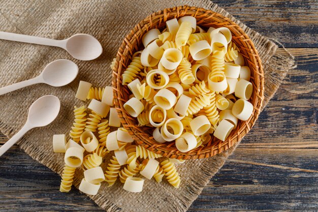 Macaroni pasta in a bowl with spoons flat lay on a sackcloth and wooden background