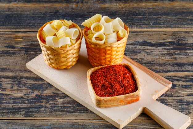 Macaroni pasta in buckets with red spice on cutting board and wooden background. horizontal