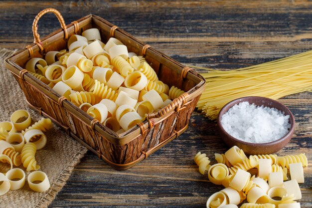 Macaroni pasta in a tray with salt, spaghetti high angle view on a wooden background