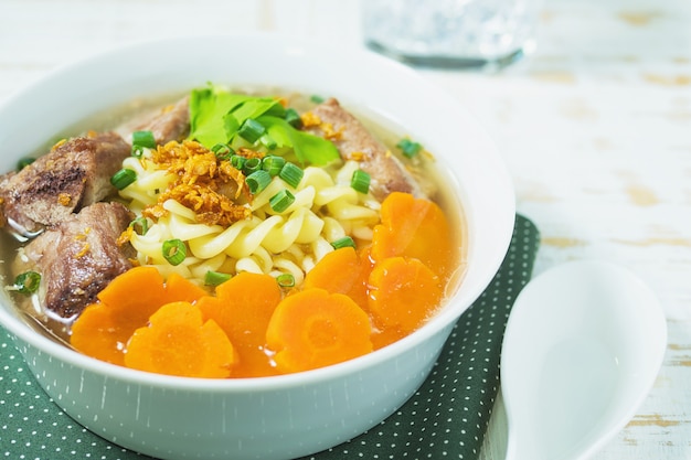 Macaroni soup with pork and carrot on white wooden table 