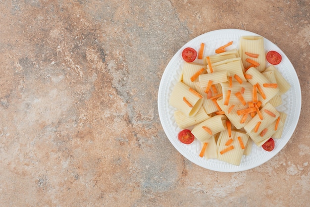 Macaroni with carrot and tomato cherry on white plate.