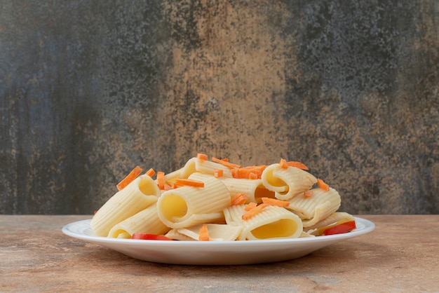 Maccheroni con carote e pomodorini sul piatto bianco.