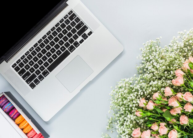 Macaroons in box; laptop and bunch of flowers on white background