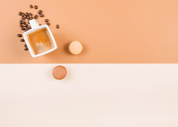 Macaroons; чашка кофе; и жареные кофейные бобы на двойном фоне