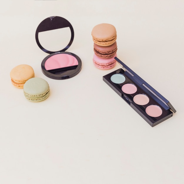 Free photo macaroons; eye shadow palette and pink blusher on colored background
