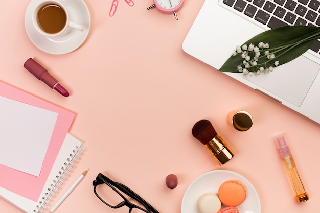 Macaroons,makeup products,spiral notepads,coffee cup and laptop on peach colored backdrop