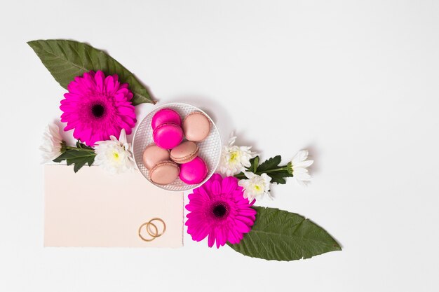 Macaroons on plate between flowers, foliage, paper and rings