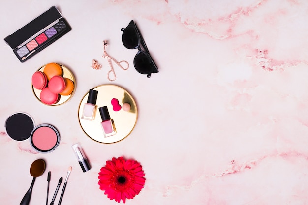 Macaroons; sunglasses and cosmetics products on pink textured background