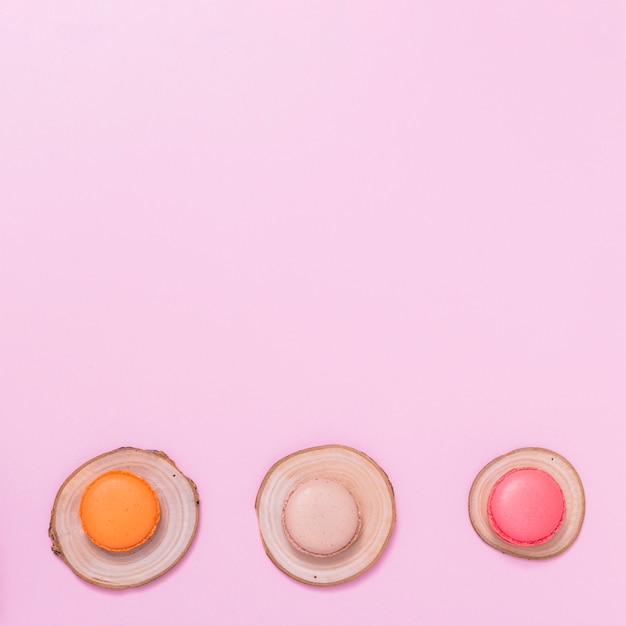 Macaroons over the tree stump against pink background with copyspace for writing the text