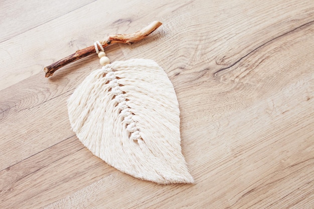 Macrame leaf  in natural color and thread windings lying on a wooden table. cotton rope decor macrame to make your room more cozy and unique. woman hobby. handmade wall hanging decor.
